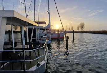 Solnedgang over vandet ved Havenlodge Lelystad i Marina Parcs Lelystad, Holland, med husbåd og lystbåde.