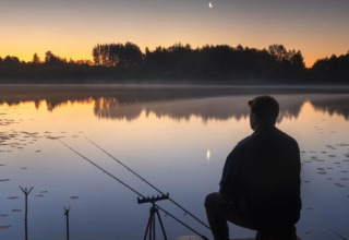 Un hombre pescando al atardecer desde una casa flotante en Havenlodge Lelystad, Marina Parcs, Países Bajos.