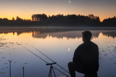 Een man vist bij schemering vanaf een havenlodge huisboot bij Marina Parcs Lelystad, Nederland.
