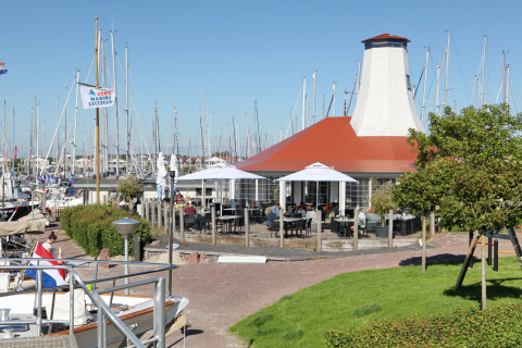Havenlodge Lelystad husbåd ved Marina Parcs i Lelystad, Holland, med både og udendørs café på en solrig dag.