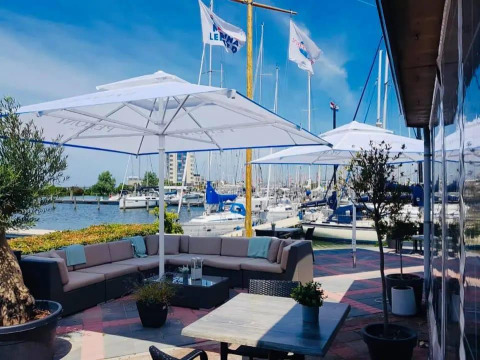 Terraza exterior en Havenlodge Lelystad con sombrillas, sofás cómodos y vistas a la marina en Marina Parcs, Países Bajos.