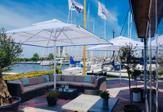 Terraza exterior en Havenlodge Lelystad con sombrillas, sofás cómodos y vistas a la marina en Marina Parcs, Países Bajos.