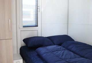 Moderne seng med mørkeblåt sengetøj i et lyst værelse på husbåden Havenlodge Lelystad i Holland.