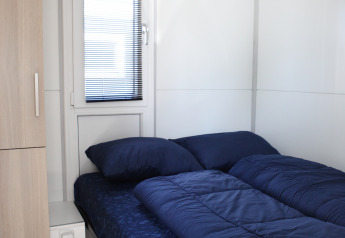Moderne seng med mørkeblåt sengetøj i et lyst værelse på husbåden Havenlodge Lelystad i Holland.