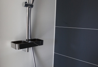 Moderne douche op een woonboot bij Havenlodge Lelystad, Marina Parcs Lelystad in Nederland met donkere tegels.