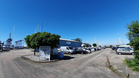 Zona de aparcamiento en Marina Parcs Lelystad, con coches, barcos y cielo azul claro en Lelystad, Países Bajos.
