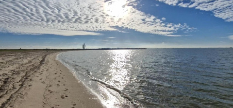 Zonnig strand met kalm water bekeken vanaf Havenlodge Lelystad bij Marina Parcs in Nederland.