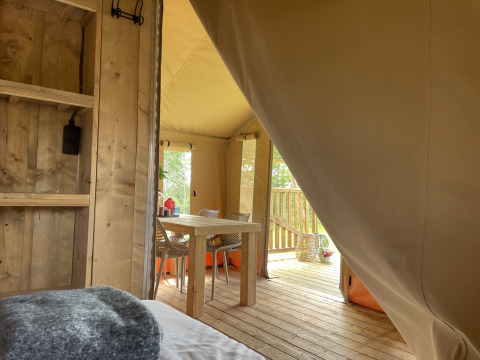 Blick aus dem Schlafbereich eines Safari-Zeltes auf Camping Le Bois de la Gachère mit Tisch und Veranda.