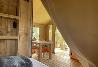 View from the sleeping area of a safari tent at Camping Le Bois de la Gachère with dining table and deck.