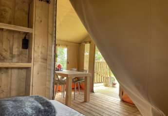 Blick aus dem Schlafbereich eines Safari-Zeltes auf Camping Le Bois de la Gachère mit Tisch und Veranda.