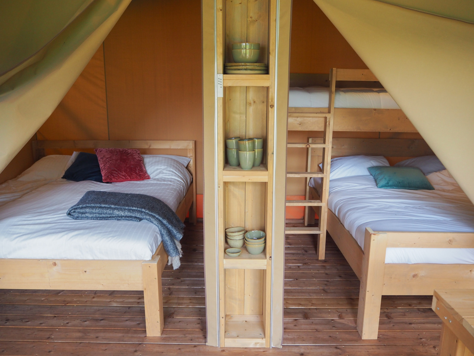 Interieur van een safaritent op Camping Le Bois de la Gachère in Frankrijk met bedden en houten vloer.