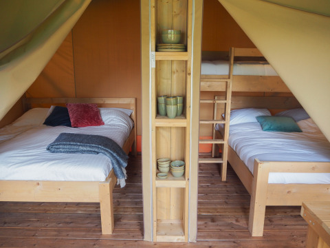 Interieur van een safaritent op Camping Le Bois de la Gachère in Frankrijk met bedden en houten vloer.
