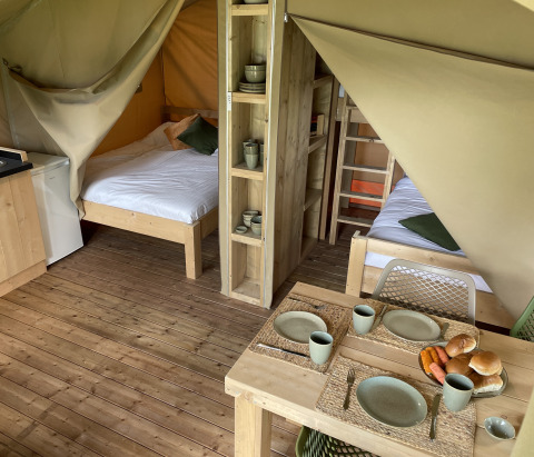 Indvendigt udsyn fra en safaritelt ved Camping Le Bois de la Gachère i Frankrig med senge og spisebord.