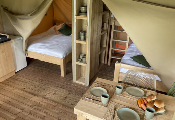 Interior view of a safari tent at Camping Le Bois de la Gachère in France, showing beds and dining area.