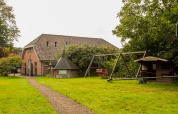 Legeplads og landligt feriehus ved Feather Down Het Boshuis feriepark i Gelderland, Holland, omgivet af grønt.