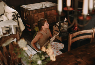 Ragazza che tosta un marshmallow vicino a una stufa a legna in un accogliente alloggio glamping in un villaggio vacanze.