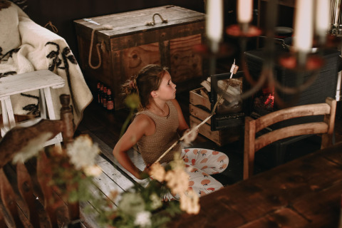 Girl toasting marshmallow by a wood stove inside a cozy glamping accommodation at a holiday park.