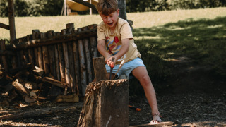 Un niño corta leña al aire libre en Feather Down Het Boshuis, un parque de vacaciones en Gelderland, Países Bajos.
