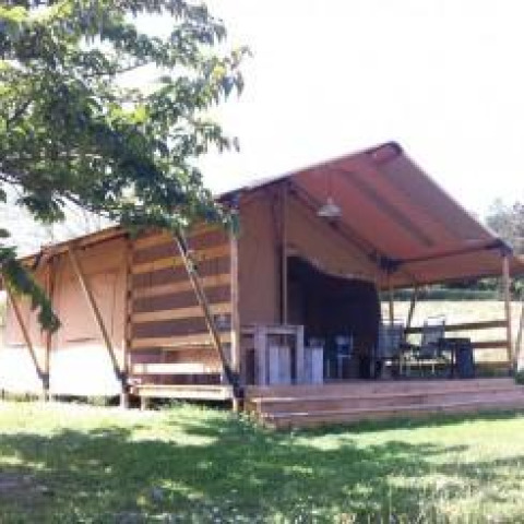 Safari-Zelt mit Holzterrasse und Sitzbereich im Freien, gelegen auf einer grünen Wiese bei Sonnenschein.