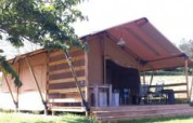 Tenda safari con terrazza in legno e tavoli all’aperto, immersa nel verde in una giornata di sole.