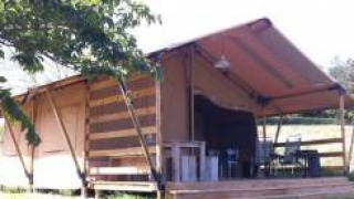 Tenda safari con terrazza in legno e tavoli all’aperto, immersa nel verde in una giornata di sole.