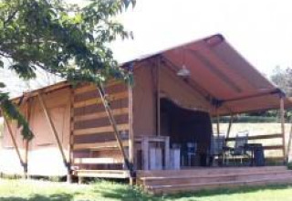 Tienda safari con terraza de madera y muebles exteriores, rodeada de césped verde en un día soleado.