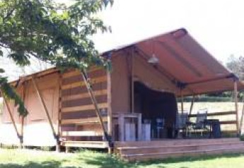 Tenda safari con terrazza in legno e tavoli all’aperto, immersa nel verde in una giornata di sole.