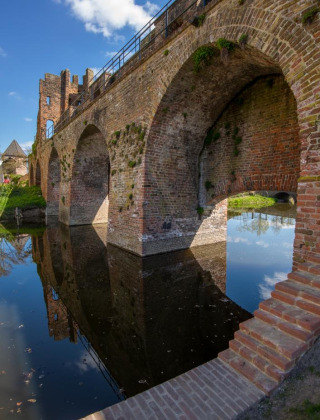 Puente de piedra histórico reflejado en el agua cerca de Vierakker, Güeldres, Países Bajos, día soleado.
