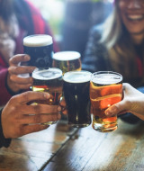 Vrienden klinken met bier aan een tafel in een vakantiepark met glamping, vrolijk samenzijn.