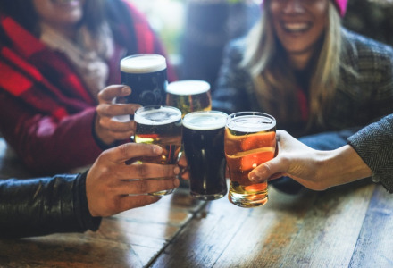 Amigos brindando con cerveza sobre una mesa de madera en un parque vacacional con glamping.