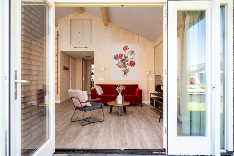 Vista de entrada al Eneva disabled lodge en Tusken de Marren, con sofá rojo y arte floral en la pared en Países Bajos.