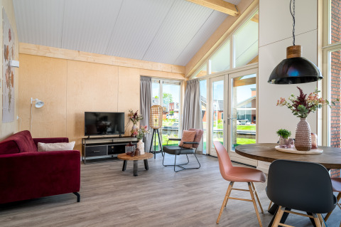 Stijlvolle leefruimte in Eneva disabled lodge, Tusken de Marren, Nederland, met grote ramen en zicht op het water.