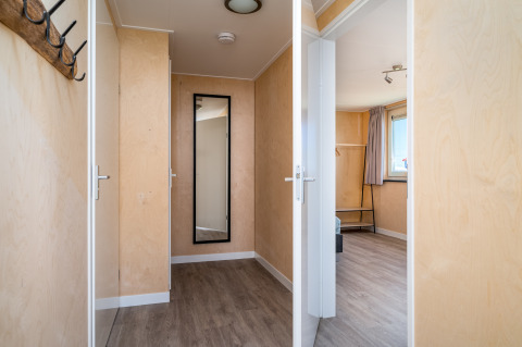 Heldere gang met houten vloer, spiegel en slaapkamer in Eneva disabled lodge bij Tusken de Marren.