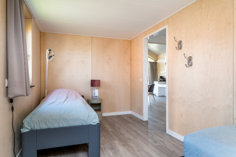Chambre accessible à la lodge Eneva, Tusken de Marren, Pays-Bas, lit simple et murs en bois clair, vue cuisine.