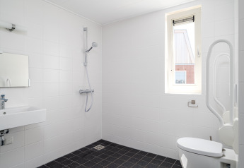 Badeværelse med handicapvenlige faciliteter inklusive bruser, toilet med støttegreb og vask.