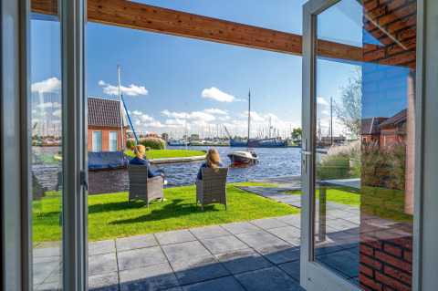 Uitzicht vanuit Eneva disabled lodge bij Tusken de Marren, Nederland, met mensen en boten aan het water.