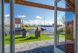Uitzicht vanuit Eneva disabled lodge bij Tusken de Marren, Nederland, met mensen en boten aan het water.