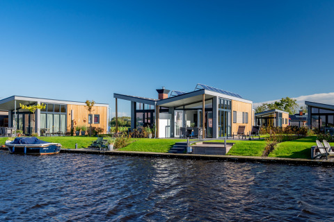 Moderne lodges aan het water bij Knilles, Tusken de Marren, Nederland, met een boot en blauwe lucht.
