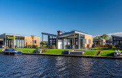 Moderne lodges aan het water bij Knilles, Tusken de Marren, Nederland, met een boot en blauwe lucht.