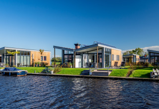 Moderne lodges aan het water bij Knilles, Tusken de Marren, Nederland, met een boot en blauwe lucht.