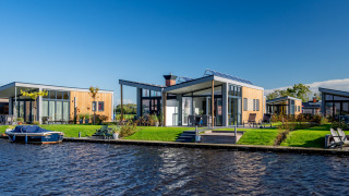 Moderne lodges aan het water bij Knilles, Tusken de Marren, Nederland, met een boot en blauwe lucht.