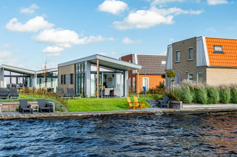 Moderne Knilles-lodge aan het water bij Tusken de Marren, Nederland, met tuin en zitplekken buiten.