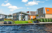 Moderne Knilles-lodge aan het water bij Tusken de Marren, Nederland, met tuin en zitplekken buiten.