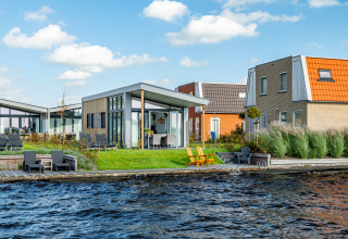 Moderne Knilles-lodge aan het water bij Tusken de Marren, Nederland, met tuin en zitplekken buiten.