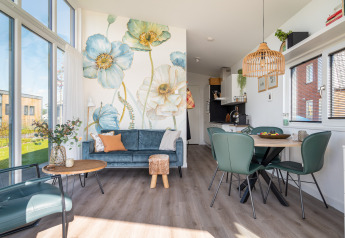 Interior moderno y luminoso de una cabaña con sofá azul, mural floral y zona de comedor junto al agua en Knilles.