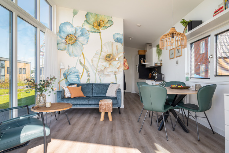 Interior moderno y luminoso de una cabaña con sofá azul, mural floral y zona de comedor junto al agua en Knilles.