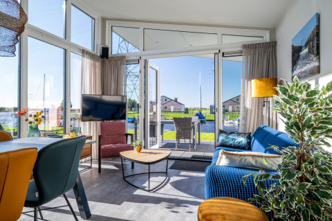 Lichte woonkamer in Knilles-lodge aan het water bij Tusken de Marren, Nederland, met uitzicht op het terras.