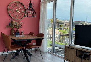 Moderne woonkamer met grote ramen, roze muur, eettafel en uitzicht op het water bij Knilles, Tusken de Marren.