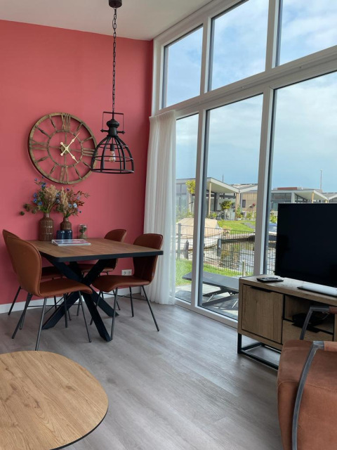 Moderne stue med store vinduer, pink væg, spisebord og udsigt over vand ved Knilles lodge, Tusken de Marren.