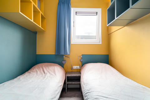 To enkeltsenge på et lille værelse med gule vægge og blå accenter i Knilles ved Tusken de Marren, Holland.